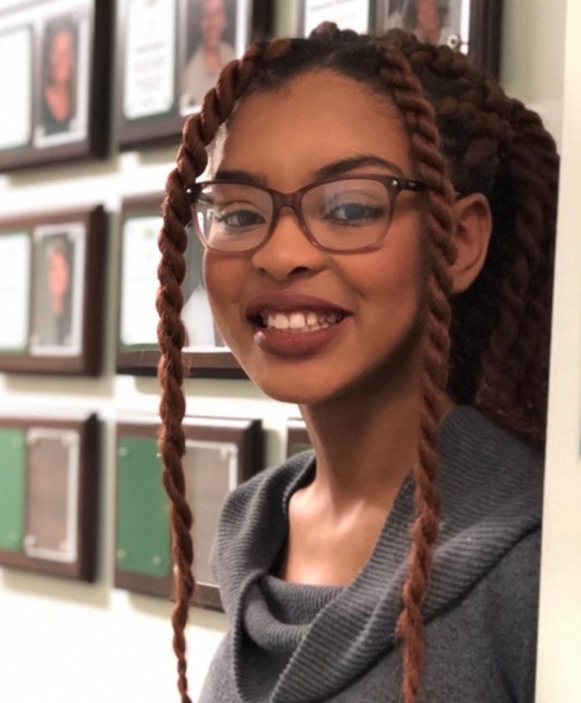 woman wearing glasses and a gray shirt with a bunch of square picture frames in the background