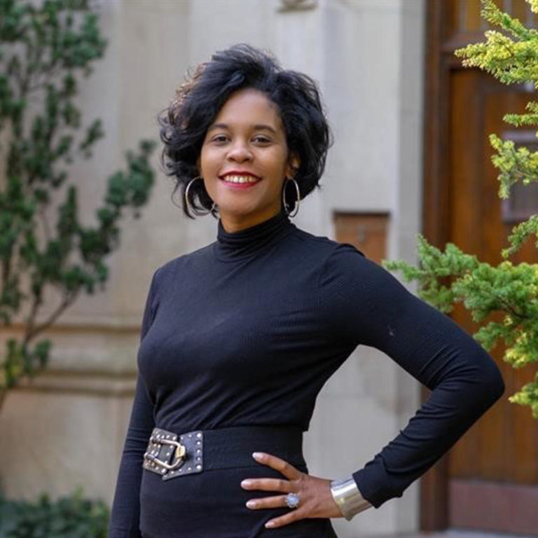 a woman with short dark hair wearing a black long sleeve turtleneck with hoop earrings 