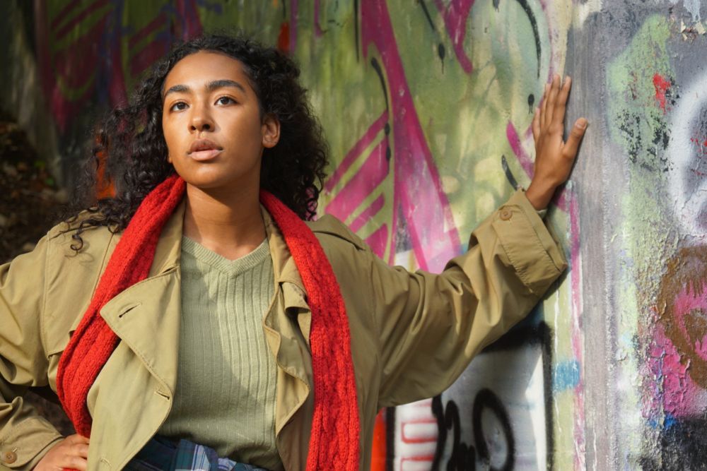 Woman leaning her hand against a wall covered in graffiti looking into the distance.