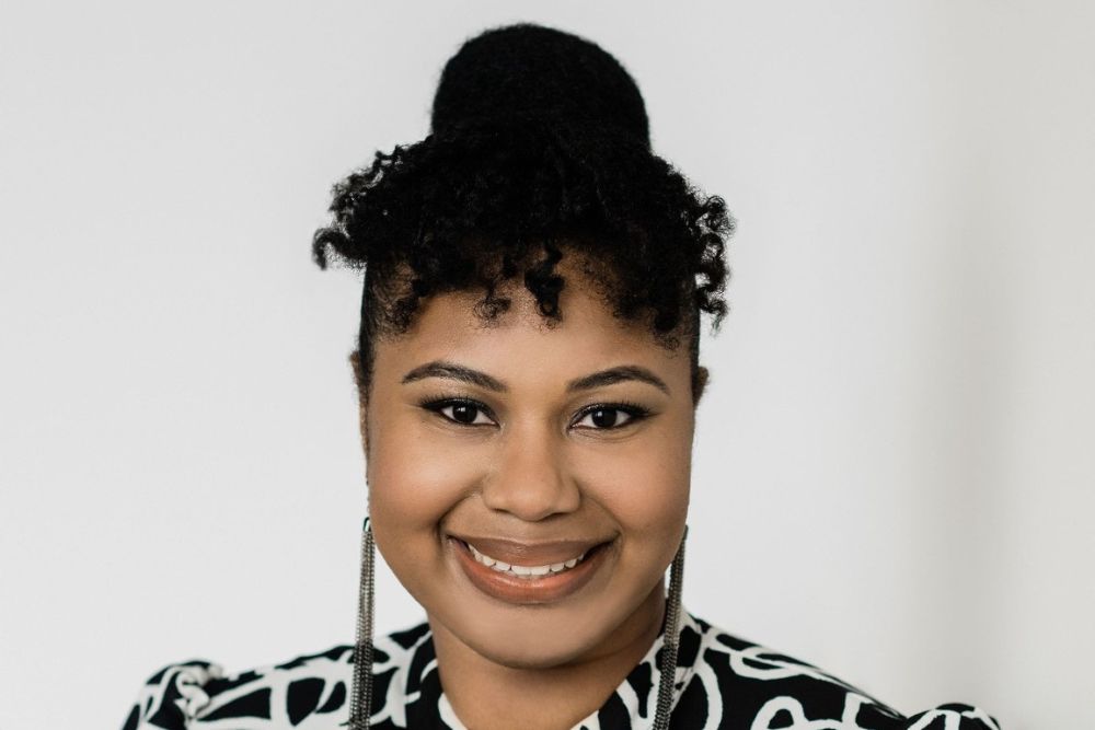 A portrait of a smiling woman with curly, dark hair wearing long earrings and a black-and-white blouse.