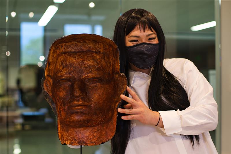 a woman with long dark hair standing next to a statue of a head