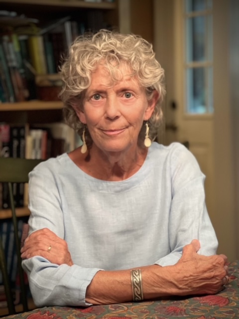 A picture of a woman in a white sweater before a bookcase.