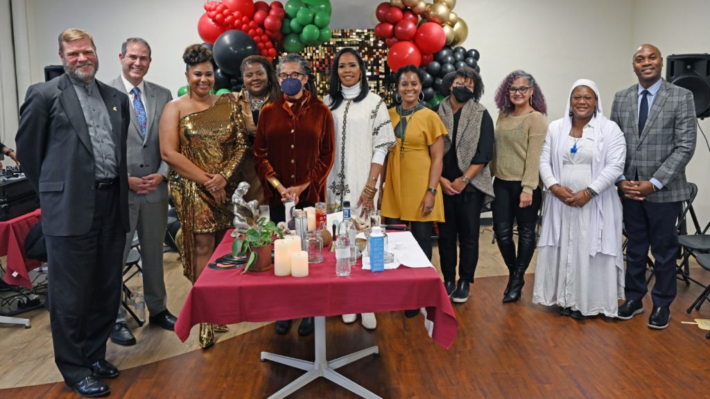 A picture of a group of people standing in front of a table with drinks on it and balloons in the background.