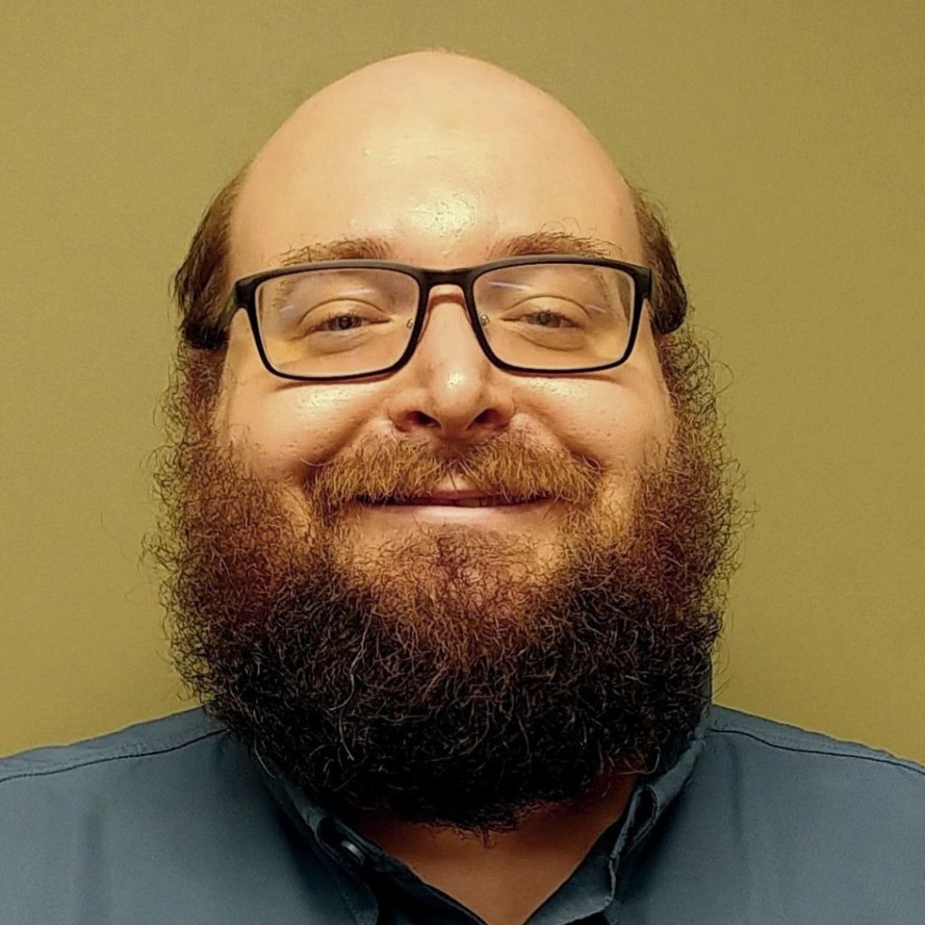 Portrait of a smiling man with beard and eyeglasses wearing a blue button-down.