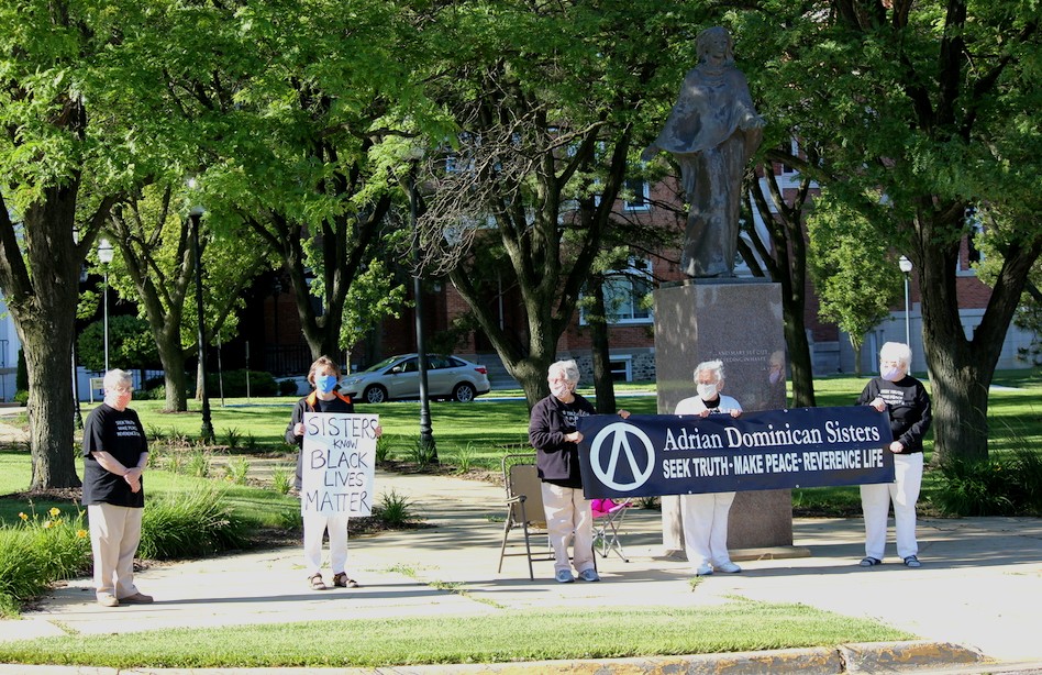Five people standing outdoors in front of a statue with signs.