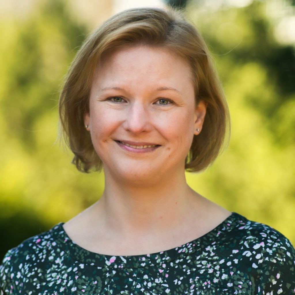 Portrait of a smiling woman with short blonde hair wearing a printed shirt.