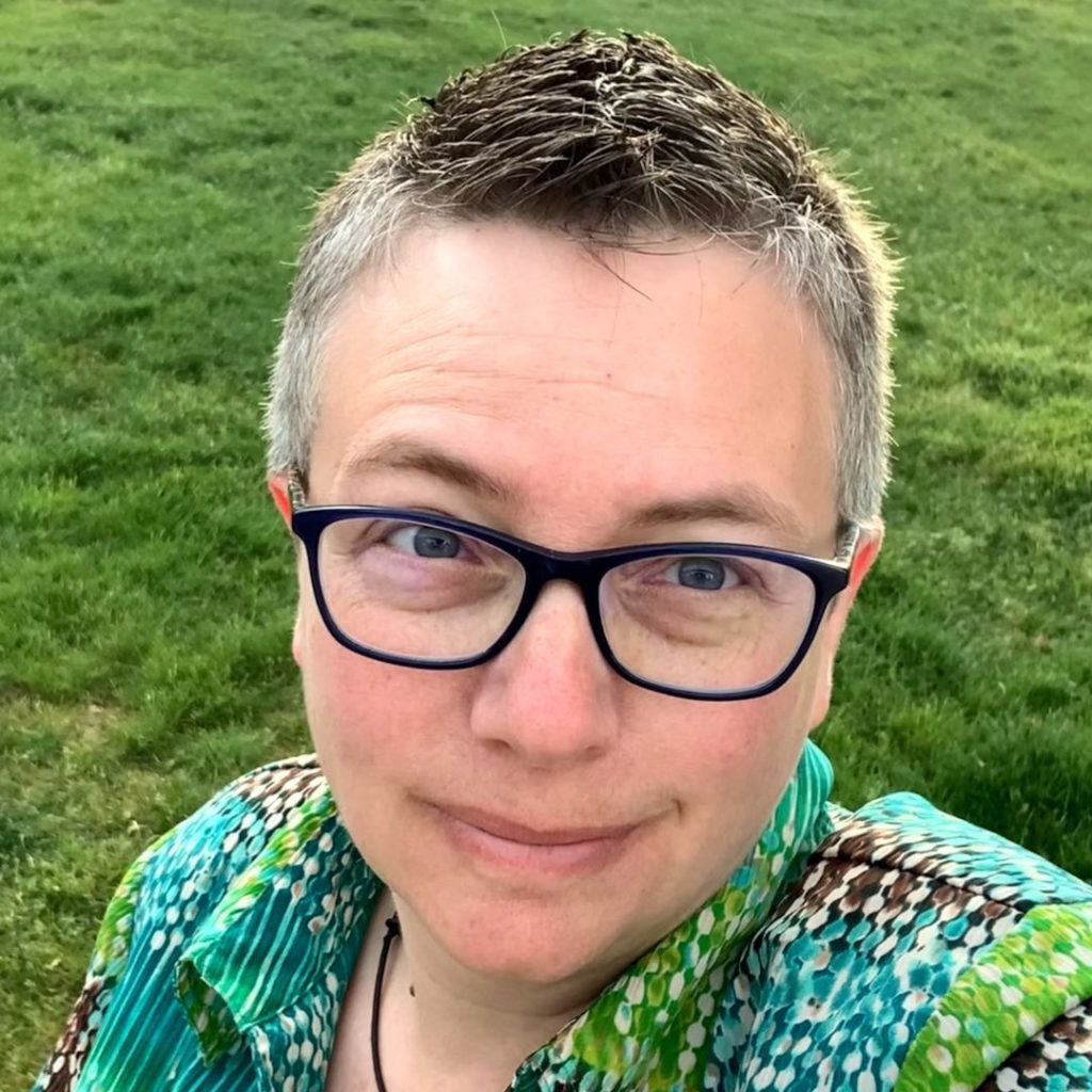 Portrait of a smiling woman with short hair and eyeglasses wearing a green printed blouse.